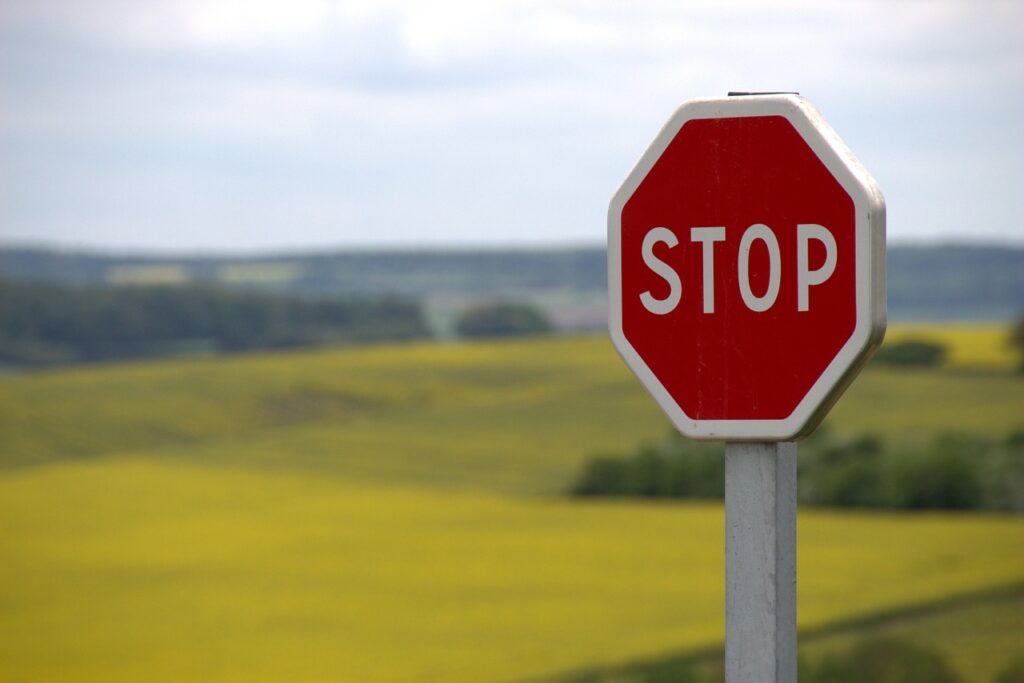 Wooden red stop sign in focus with fields and trees blurred in background