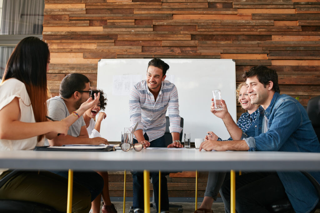Happy young people sitting around conference table at a meeting